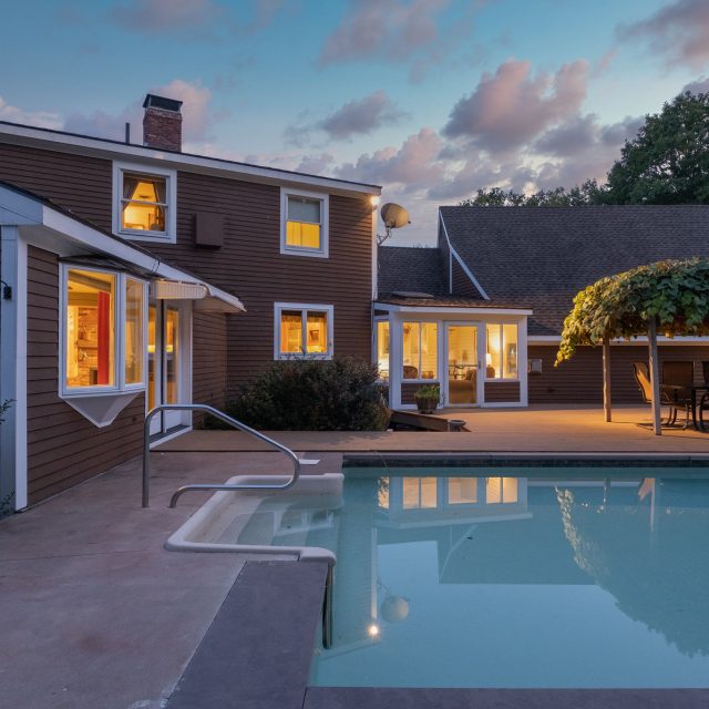 A modern cozy lit house and a pool under a cloudy sky in the evening